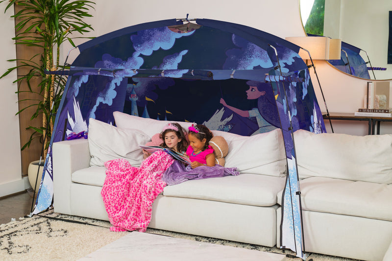 Two children on a couch under a princess-themed tent in a living room.